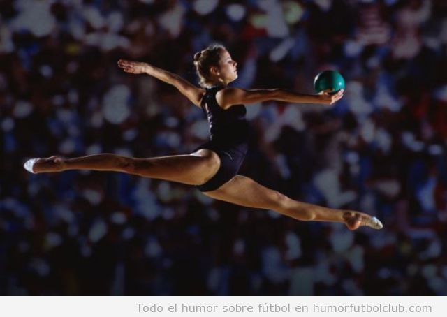 Foto de una bella gimnasta haciendo espagat en el aire con pelota gimnasia rítmica